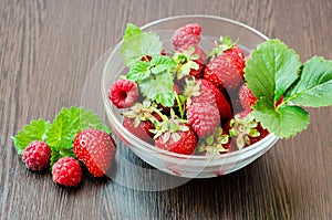 Side view of a bowl of strawberries and raspberries with mint leaves.