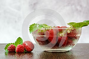 Side view of a bowl of strawberries and raspberries with mint leaves. Berries lie next to the bowl