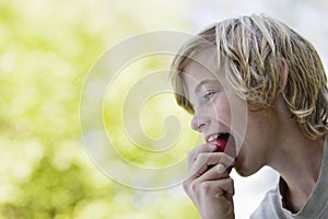Side View Of Boy Eating Apple Outdoors