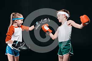 Side view of boy and girl in sportswear boxing isolated on black