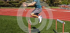 Side view of a boy jumping over a track hurdle