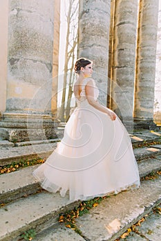 The side view of the bride in the long pompous dress standing on the stairs of the ancient building.