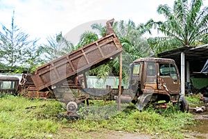 Side view of a broken down brown truck with it's container half lifted taken in the midday