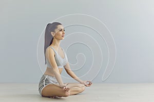 Side view of brunette in lotus position. Woman in yoga meditation, grey background, copy-space.