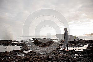 Side view brunette man standing in the black swimsuit with a white surf in his hands on the shore