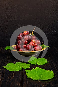 side view of a bunch of sweet grapes in a plate and green grape leaves on rustic background