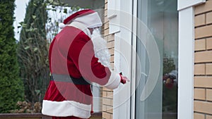 Side view burglar in red costume with white beard looking around breaking in house. Caucasian man in Santa Clause outfit