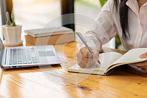 Side view of business woman's hands using laptop computer resting, young woman writing in blank notebook