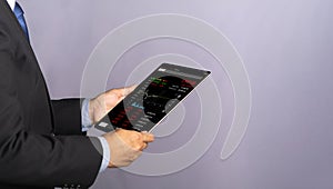 Side view of a businessman holding and reading business graphs and stock charts on a digital tablet.