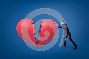 A side view of a businessman leaning forward and pushing a big red broken heart.