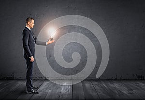 Side view of businessman standing and holding glowing light bulb in his hand