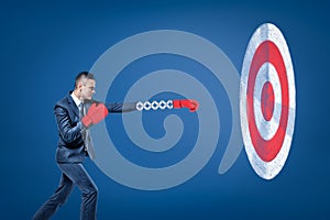 Side view of businessman wearing red boxing gloves and holding out one hand towards big round target.