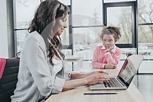 Side view of businesswoman typing on laptop while daughter getting bored