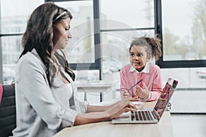 Side view of businesswoman typing on laptop while daughter getting bored