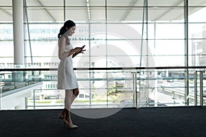 Side view of businesswoman using mobile phone in office and walking on a carpet walkway