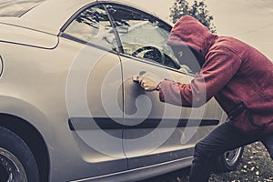 Side view of car being forced by a man in hoodie and mask. Thief tries to steal vehicle from a parking. Young male acts