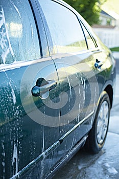 Side view of a car that is being washed. Soap suds and bubbles on the side of a wet car being cleaned