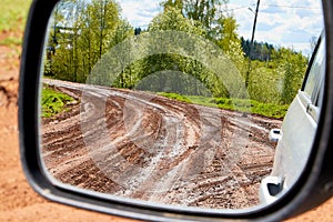 Side view with car rear view mirror on dirty clay road surrounded in natural landscape in a suumer day