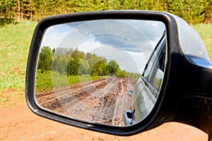 Side view with car rear view mirror on dirty clay road surrounded in natural landscape in a suumer day