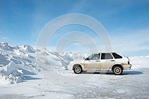 Side view of a car standing by a huge snowdrift formed after cleaning roads. The concept of cleaning roads from snow
