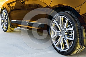 Side view of a car. Tire and alloy wheel of a modern gold car on the ground at the sunset. Car exterior details.