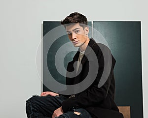 side view of casual fashion man in black coat sitting in studio