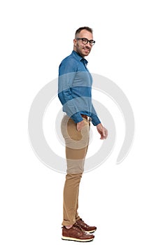 Side view of casual nerdy guy in denim shirt standing in line with hand in pocket