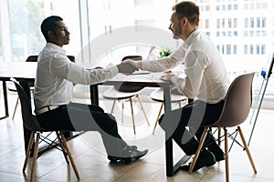 Side view of Caucasian and African American businessmen signing contract and shaking hands