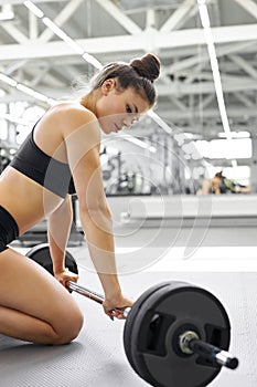 Side view on caucasian atheltic lady sitting near barbell