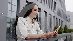 Side view Caucasian Hispanic 30s happy smiling woman standing on balcony terrace in city female businesswoman with phone