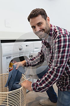 Man looking at camera while putting dirty clothes into the washing machine