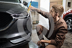 Side view of caucasian man worker of car wash service cleaning headlights of luxury grey car