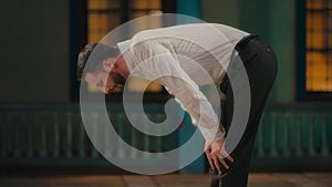 Side View of a Caucasian Muslim Man Bowing in Prayer in a Mosque at Night