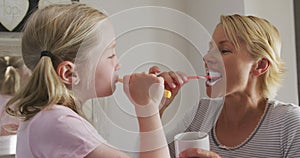 Side view of Caucasian woman and her daughter brushing their teeth