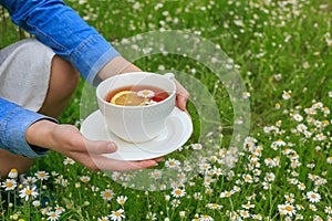 Side view caucasian woman holding in hands white cup of black tea with lemon slice, camomile flowers. Close up mug