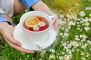 Side view caucasian woman holding in hands white cup of black tea with lemon slice, camomile flowers. Close up mug