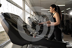 Side view of caucasian woman in sportswear adjusting speed on treadmill while exercising at gym or sport club