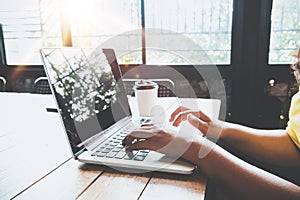 Side view of charming young hipster girl hands working on her laptop sitting at wooden table in a coffee shop.