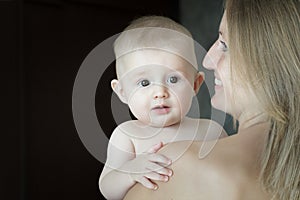 Side view of cheerful blonde woman holding her baby child