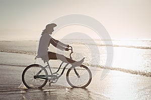 Side view of cheerful woman riding bicycle on shore at beach