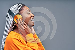 Side view of a cheerful young african woman listening to music with headphones isolated over grey background