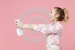 Side view of cheerful young girl housewife in casual clothes apron hold atomizer spray with washing cleanser doing