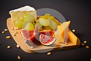 Side view of Cheese platter with cheese pieces, grapes, pine nuts segmented fig berry on wooden board