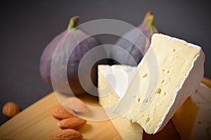 Side view of Cheese platter of Soft French Brie cheese cuts served with almond nuts and fig berries on wooden board