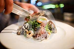 The side view of the chef cooking the seafood salad consisted of the lettuce, onion circles, mussels and octopus placed