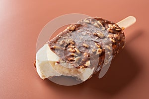 Side view chocolate outer ice cream with peanuts on brown background with some bites