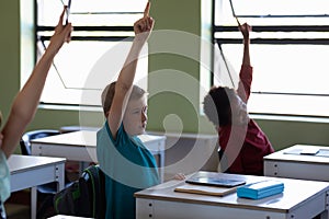 Group of school children sitting at desks and raising their hands to answer