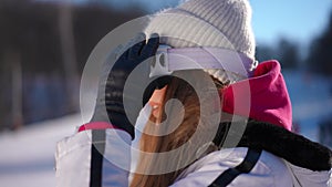 Side view close-up confident fit woman putting on ski goggles smiling standing in sunshine on winter resort. Happy