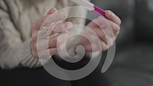 Side view close-up of female Caucasian hands holding affirmative pregnancy test. Woman with snake tattoo on finger