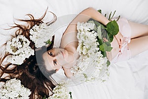 Side view close up portrait of cute millennial lady with fresh spring flowers, lying on comfy bed. Face of young cute caucasian